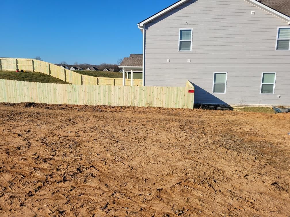 A house with a wooden fence in front of it and a dirt field in front of it.