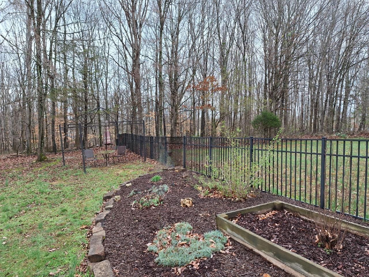 A garden with a fence and trees in the background