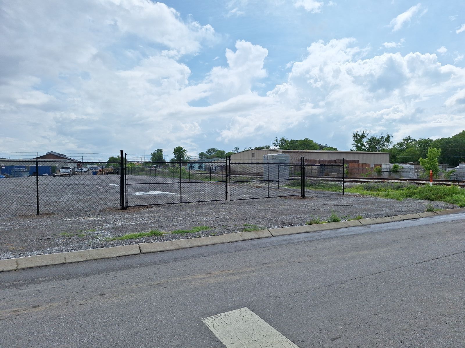 A fence surrounds a gravel lot next to a road.