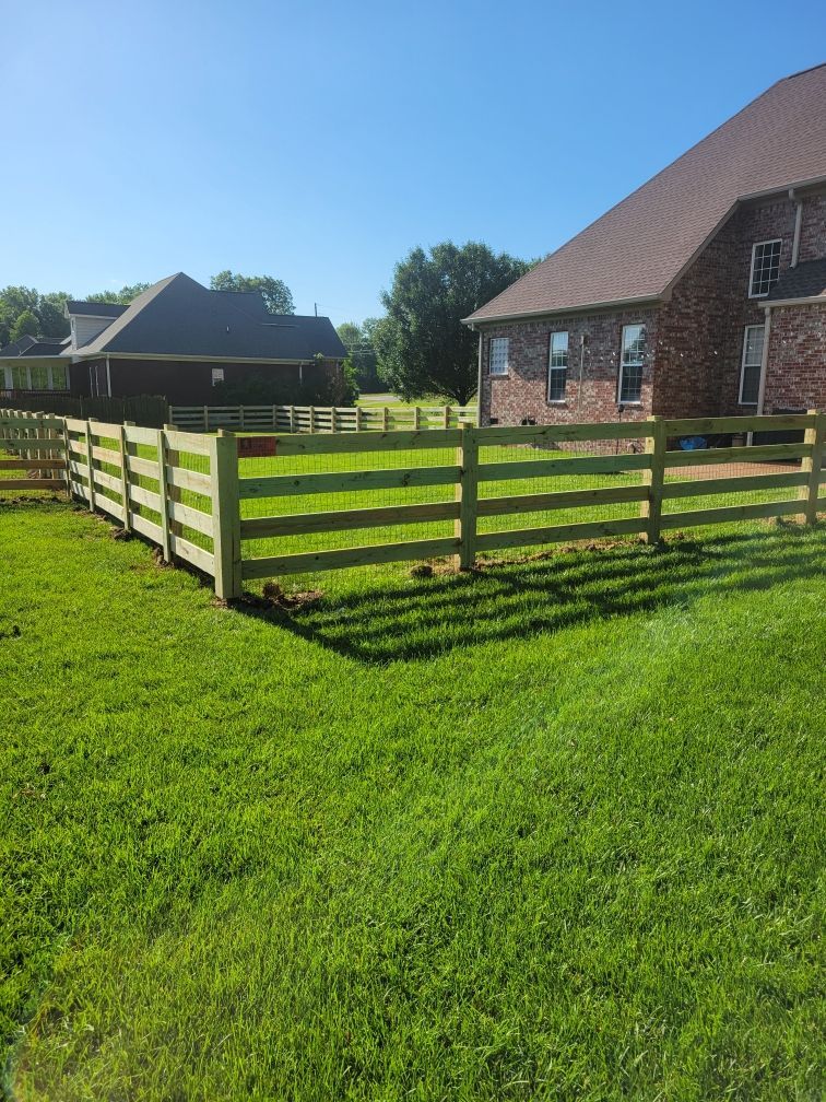 A wooden fence surrounds a lush green field in front of a house.