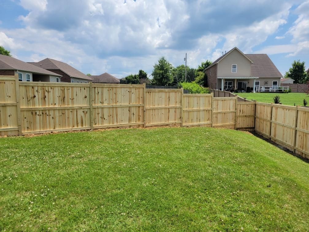A wooden fence surrounds a lush green yard in front of a house.