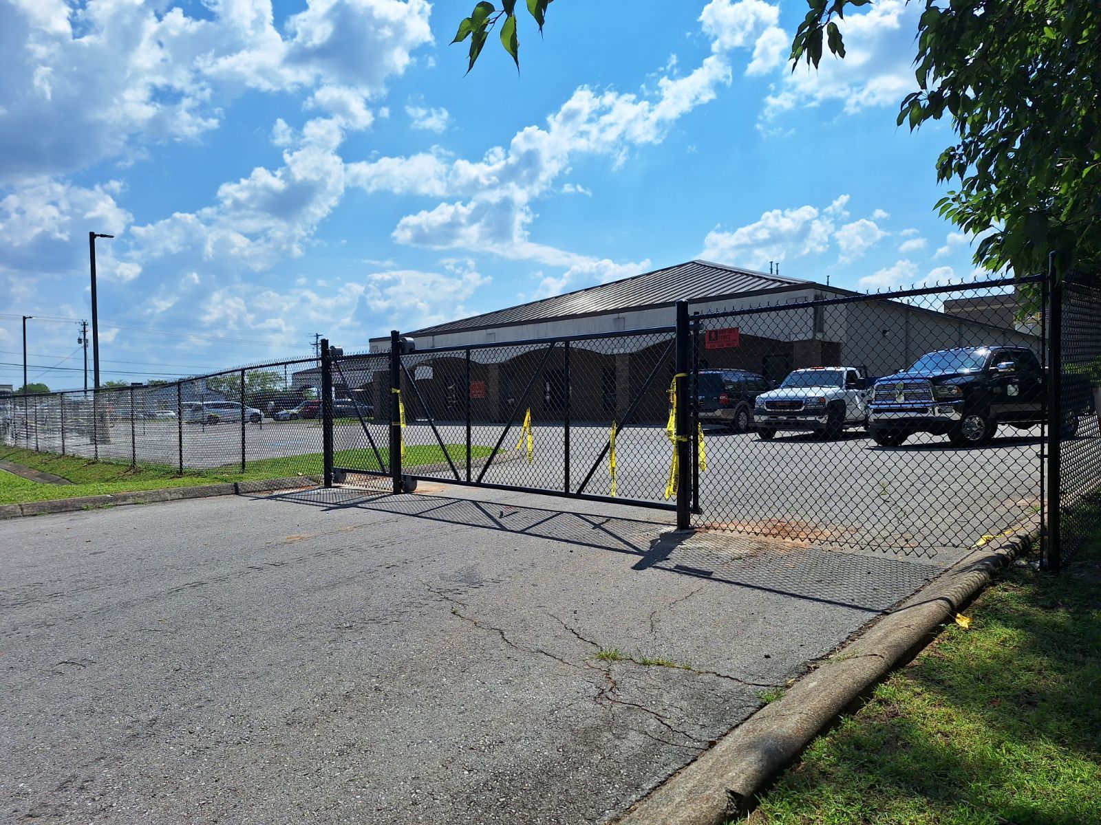 A chain link fence surrounds a parking lot with cars parked in front of it.