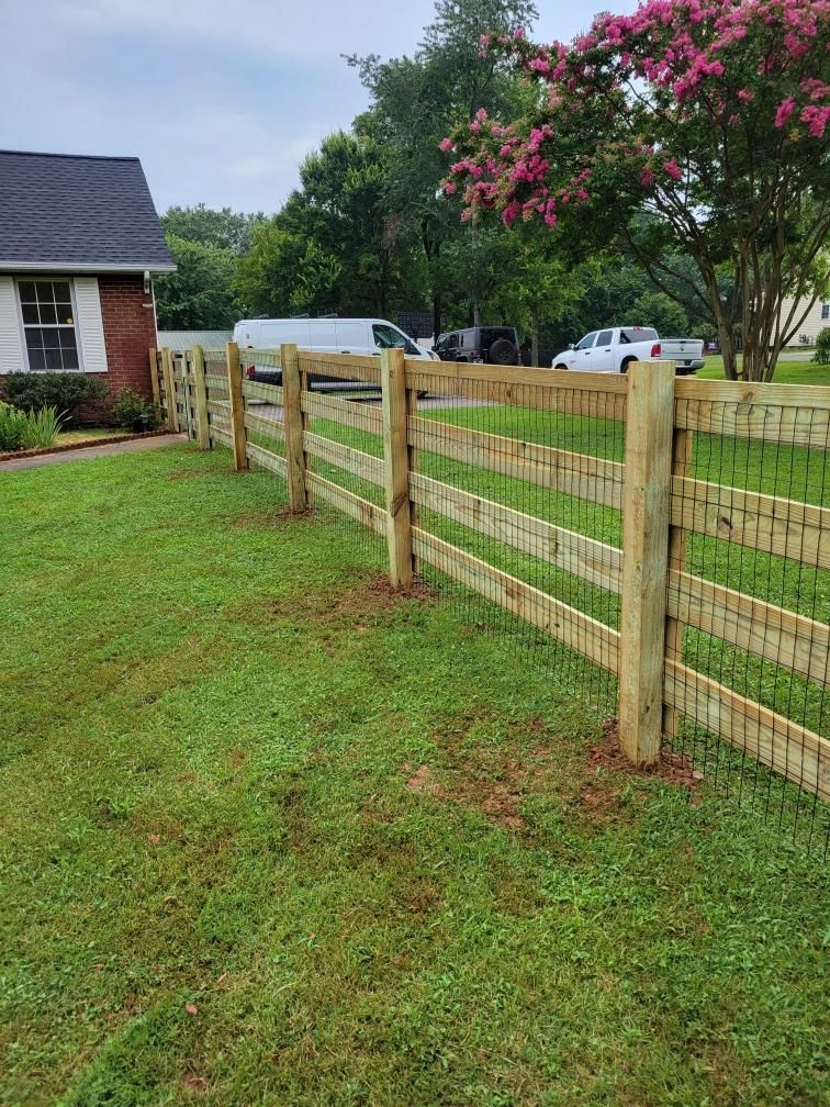A wooden fence surrounds a lush green yard in front of a house.