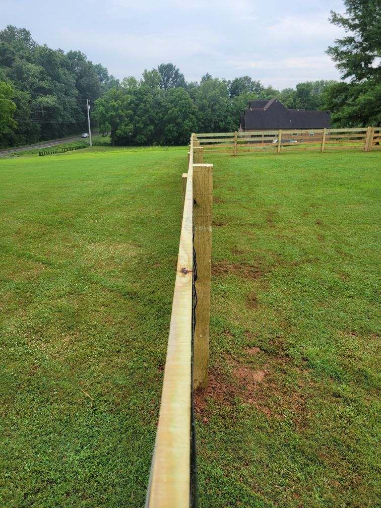 A wooden fence surrounds a lush green field.