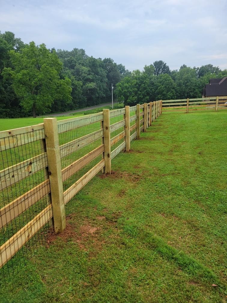 A wooden fence surrounds a lush green field.