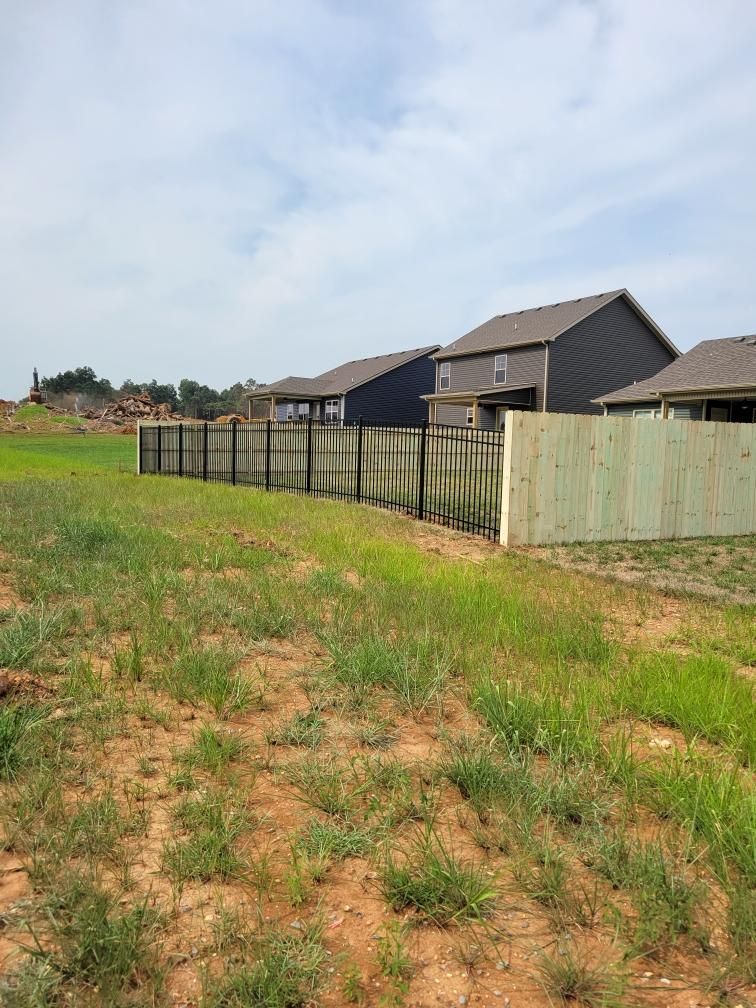A wooden fence surrounds a grassy field with houses in the background.