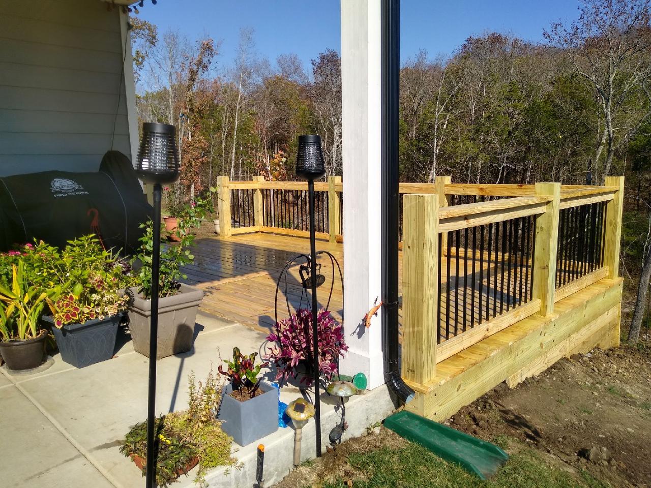 A wooden deck with a black railing is sitting next to a house.
