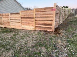 A wooden fence is sitting on top of a grassy hill next to a house.
