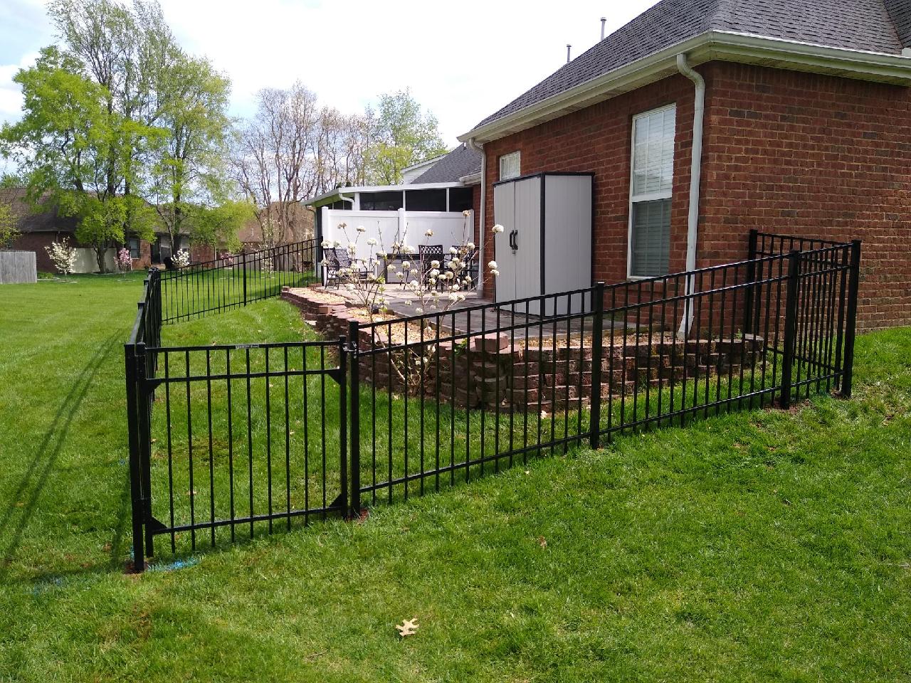 A black fence surrounds a patio area in front of a brick house.