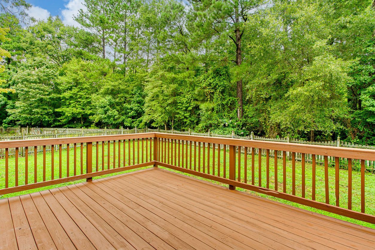 Wooden deck with brown railing overlooking a lush green backyard and trees