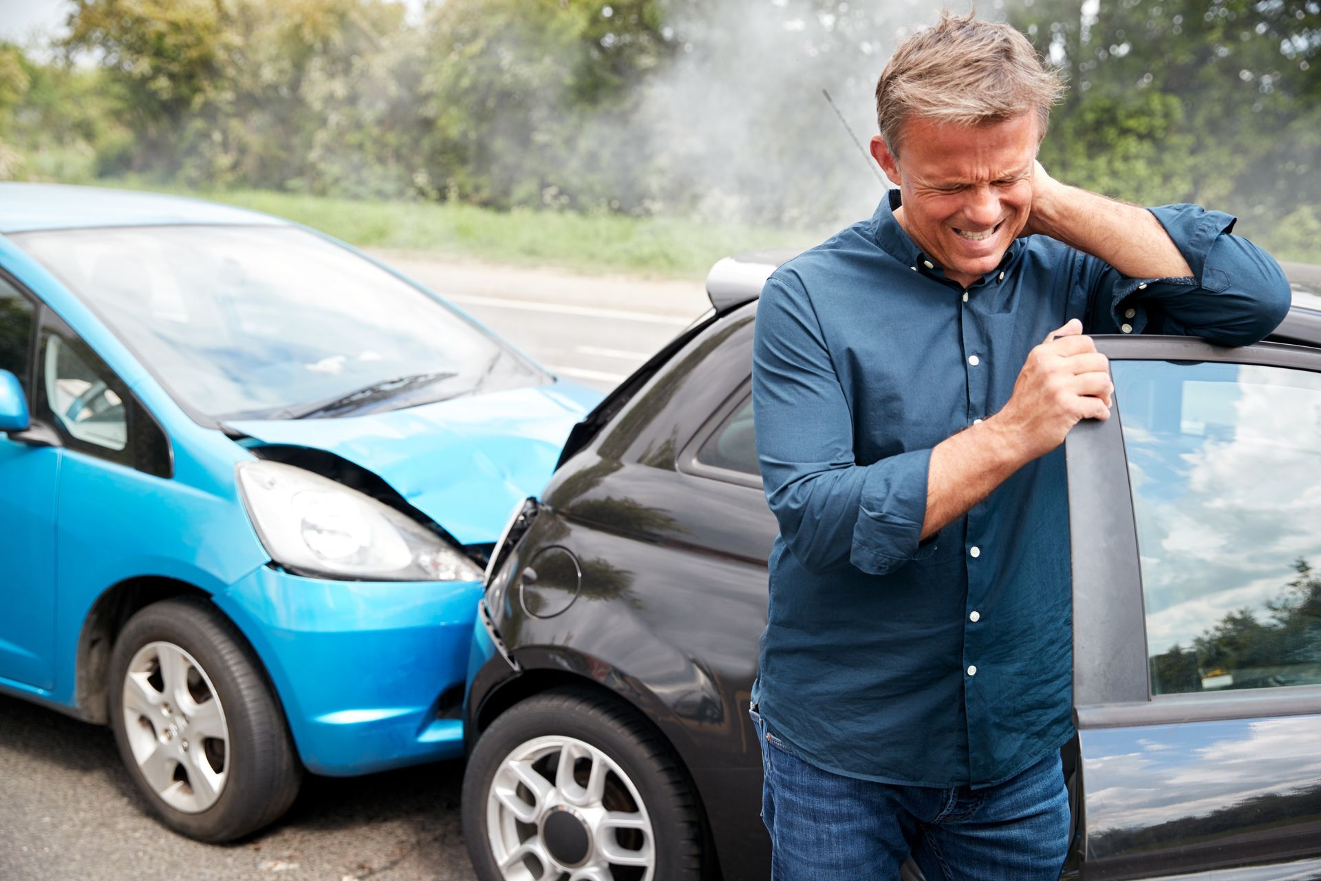 A person is standing by damaged cars after a collision, holding their neck in the accident scene.