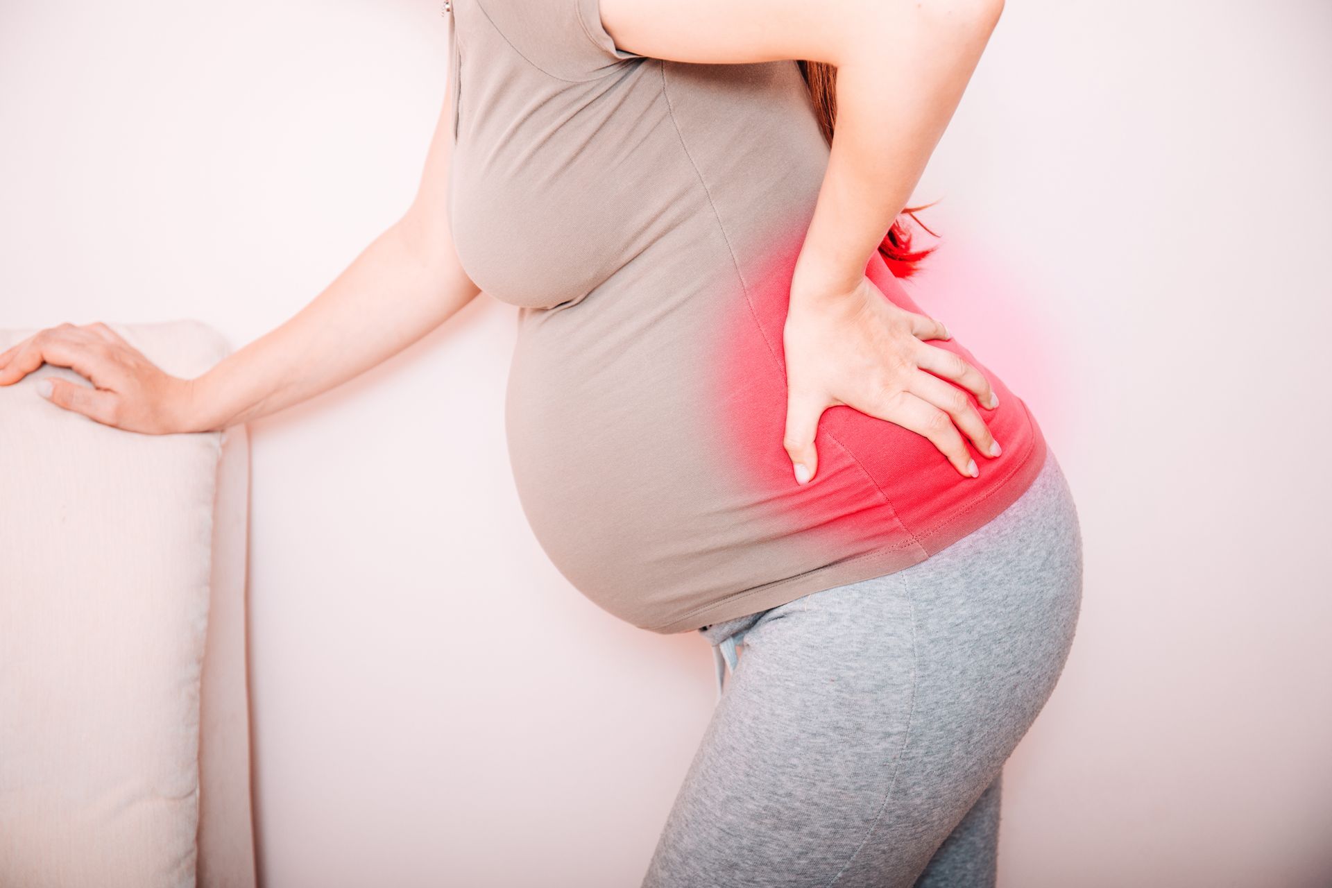 A person in their third trimester holds their lower back, which is highlighted with a red glow to indicate pain.