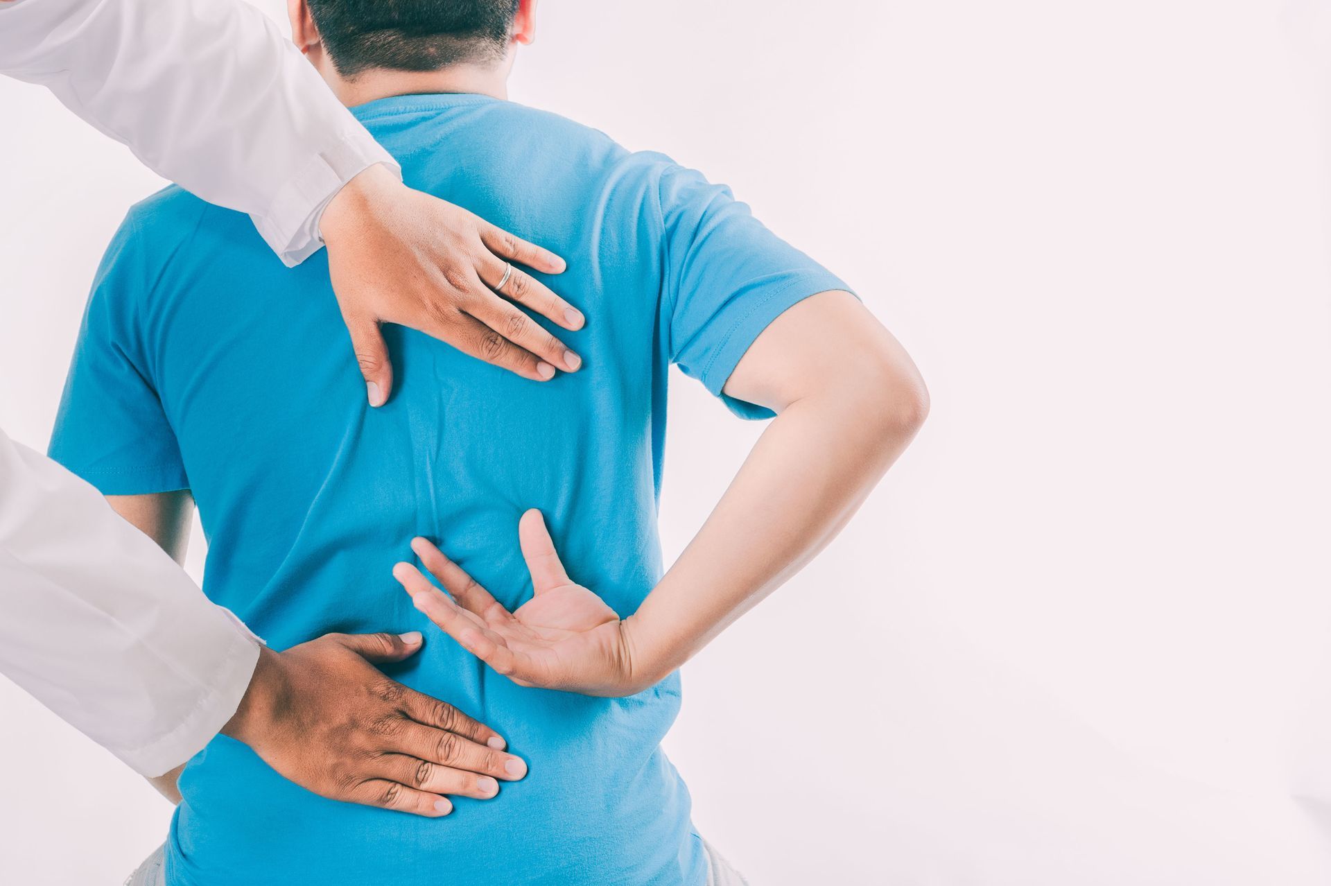 A healthcare professional in a white coat examines a patient’s back, placing hands on the upper and lower spine. A healthcare professional in a white coat examines a patient’s back, placing hands on the upper and lower spine.