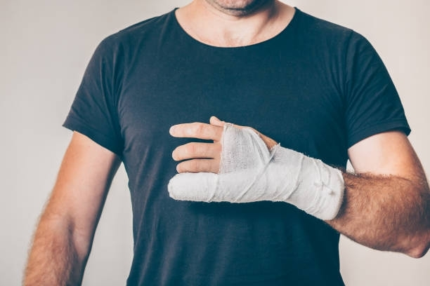 A person wearing a plain black T-shirt with their hand heavily wrapped in white medical gauze.