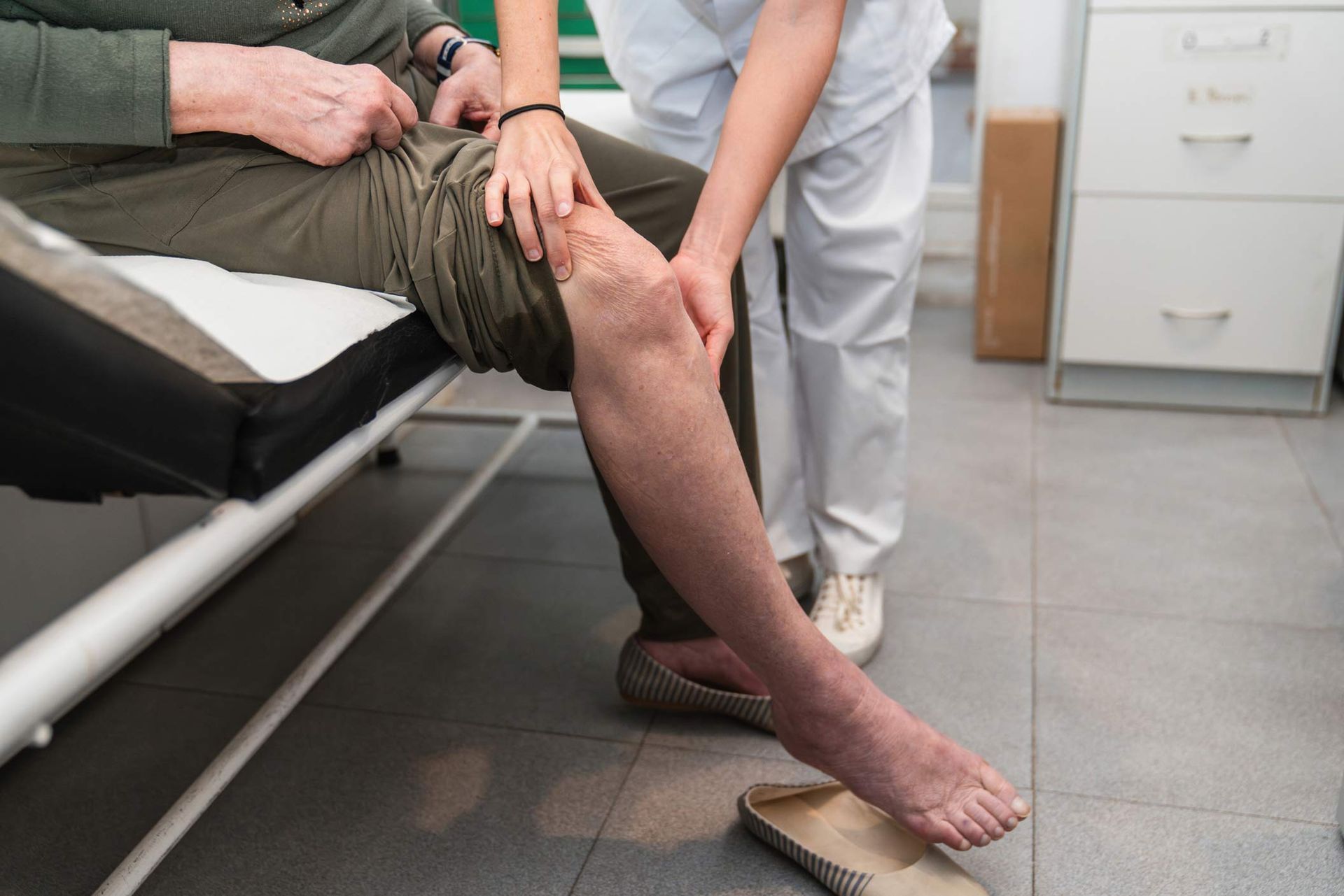 A medical professional examines a patient's knee during an appointment in a clinical office setting.