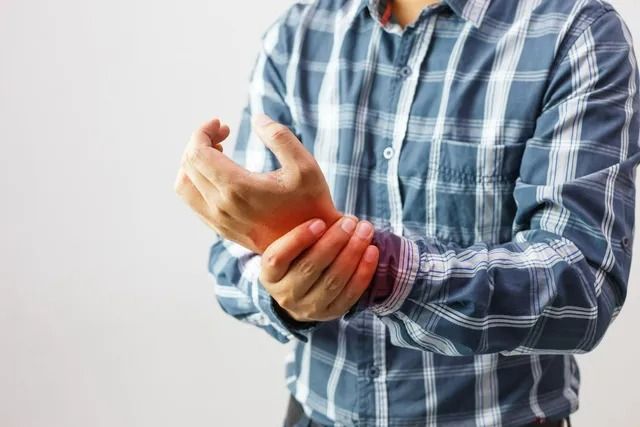 A person in a blue plaid shirt holding their wrist, which is highlighted in red to indicate pain or injury.