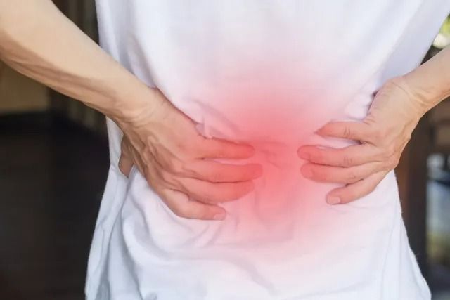A person in a white shirt holding their lower back with both hands, where a red glow indicates pain.