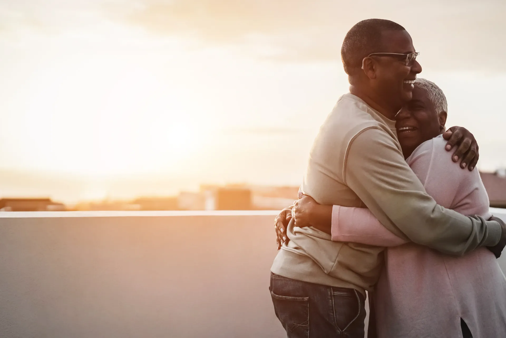 An elderly couple hugging each other on a rooftop at sunset.