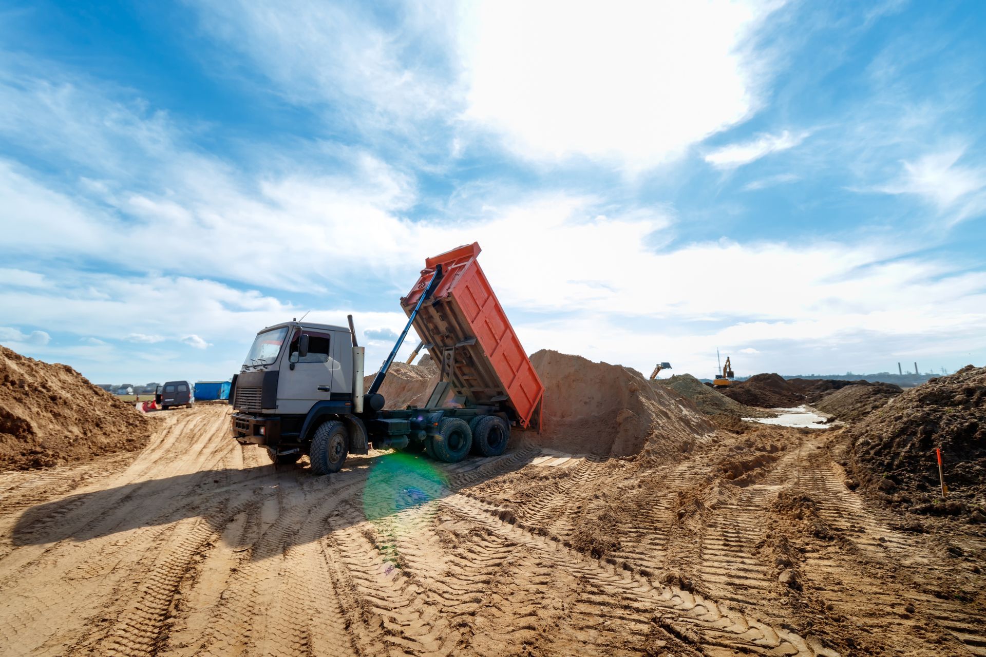 A dump truck is dumping sand on a dirt road.