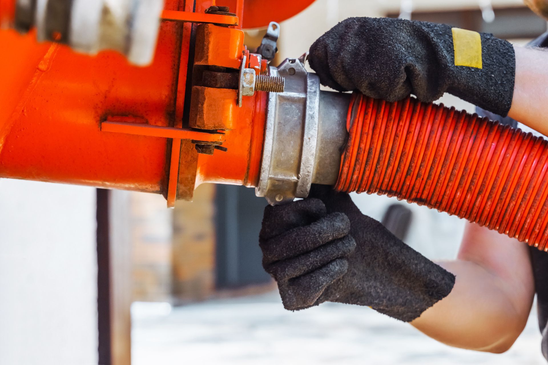 A person wearing black gloves is holding a red hose.