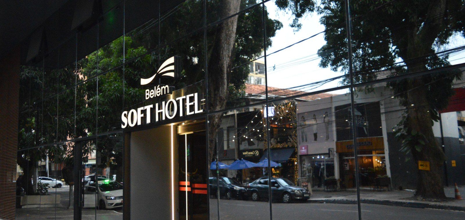 Ao entardecer, a placa do Hotel Belém Soft se destaca em uma rua arborizada e repleta de prédios.
