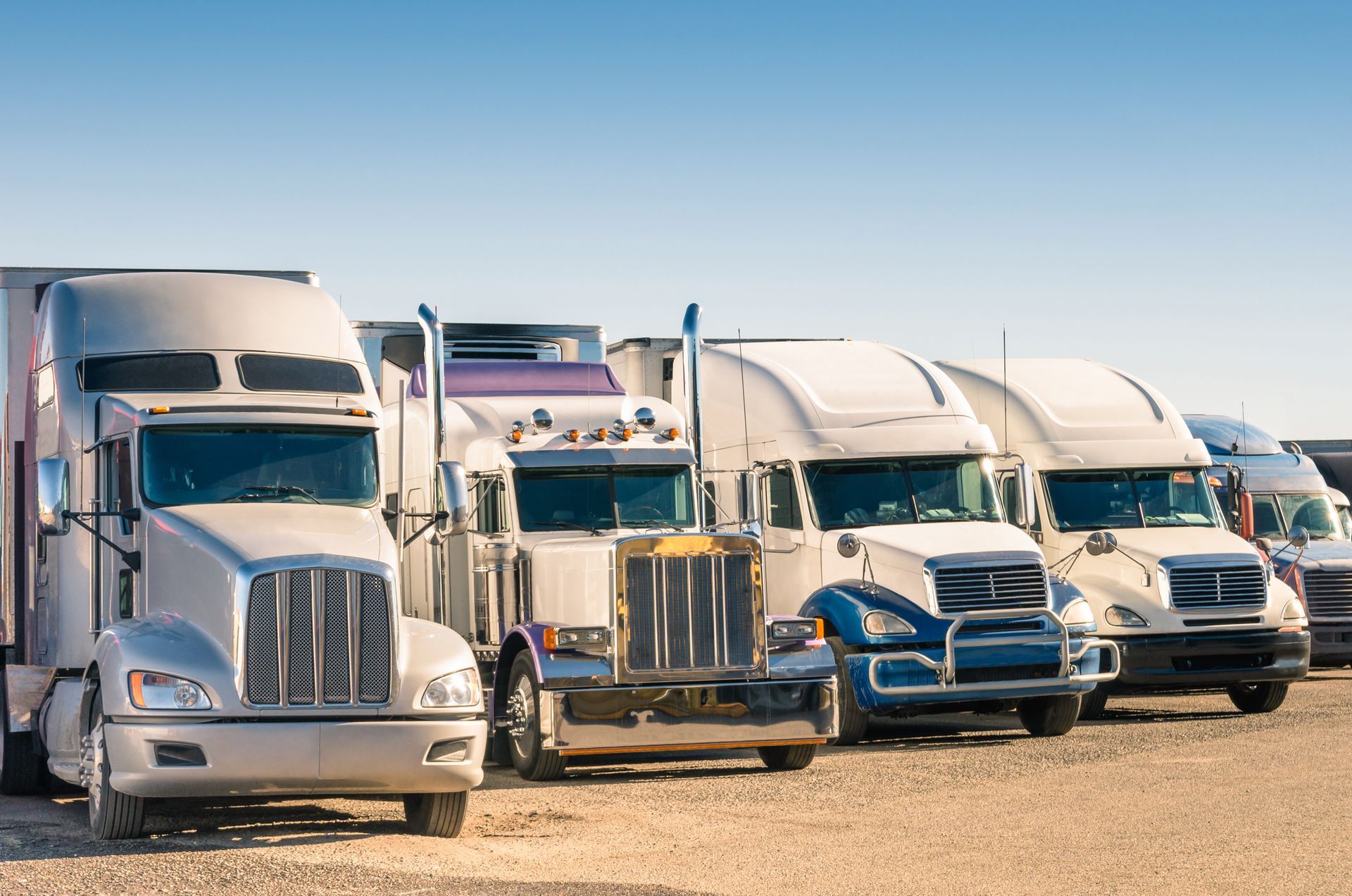 Several semi-truck tractors parked side by side in a row under a clear blue sky