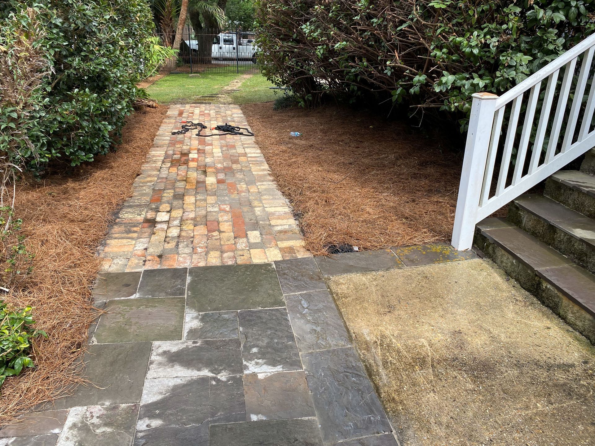 Brick walkway leading through shrubs beside a porch and stairs on a rainy day