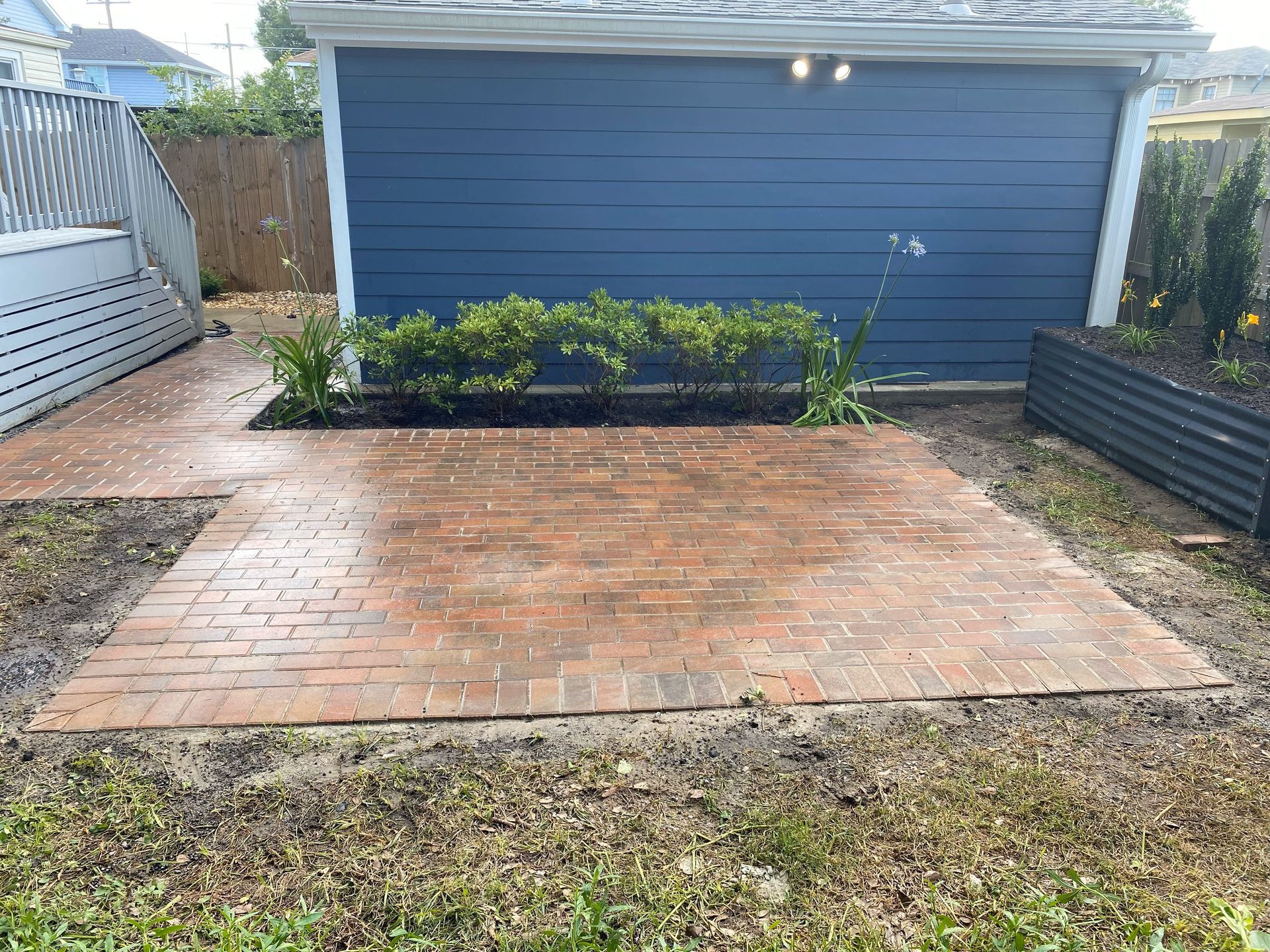 Brick patio in front of a blue garage, with low shrubs and a grass yard.