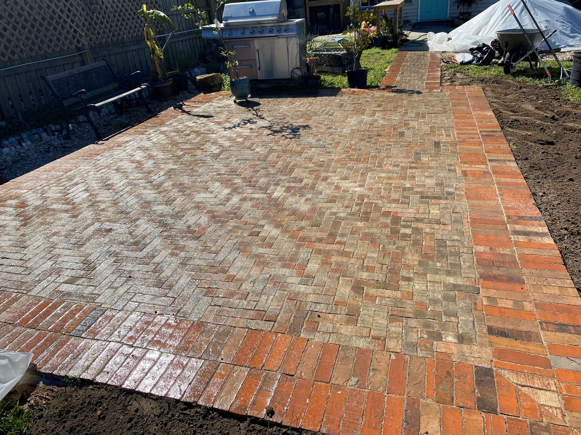 Brick-paved patio with a red brick border in a backyard, with garden items and a shed in the background