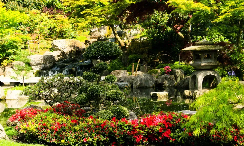There is a pond in the middle of the garden surrounded by trees and flowers.