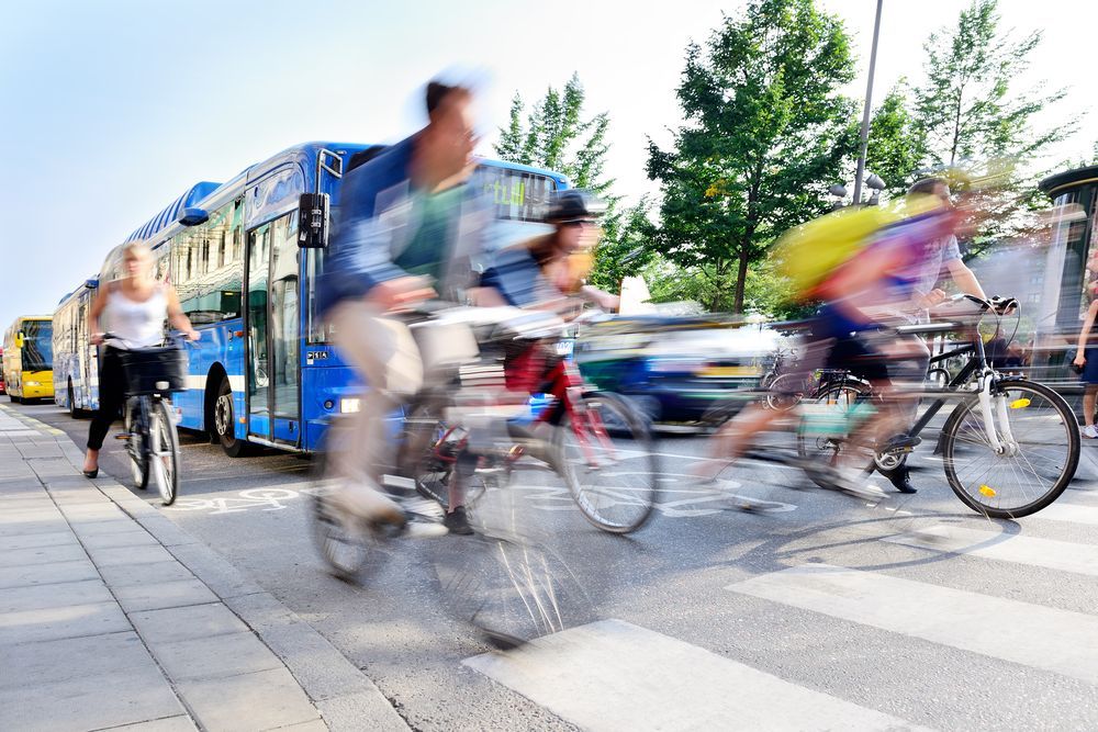 Busy city street filled with cars, pedestrians and bicycles on the road and in bike lanes.