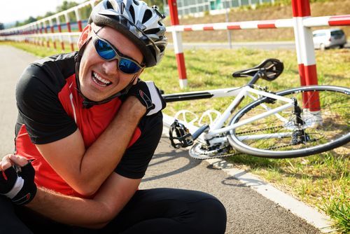 What to do after a bike accident. Injured cyclist holding shoulder after a bike crash.