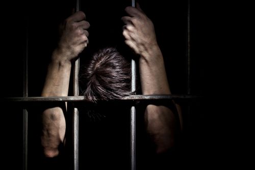 Man holding steel bars of prison cell from inside the cell