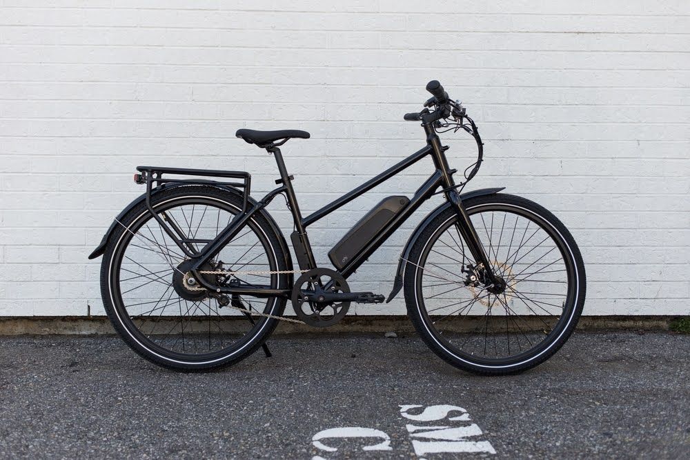Black electric bicycle leaned up against a white brick wall