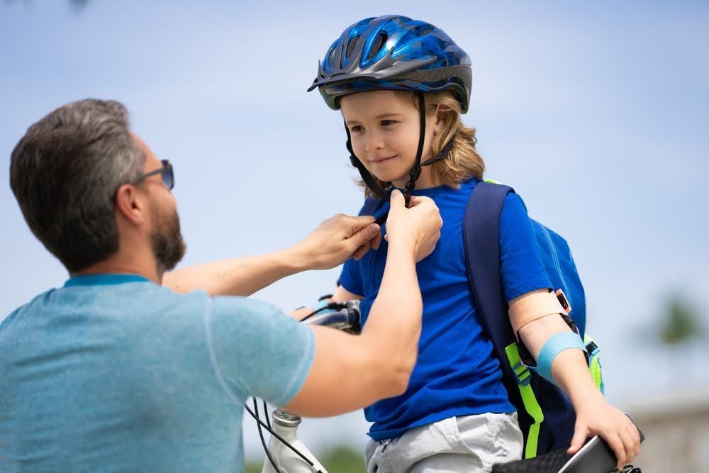 A father helping his son put on a bicycle helmet