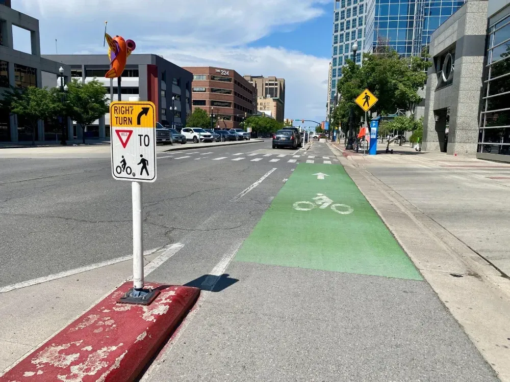 Green painted bike lane with signage for traffic to yield to bicycles and pedestrians on the road