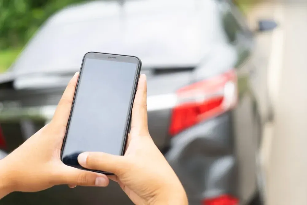 hands holding a cell phone, taking photos of an accident and damages to a car