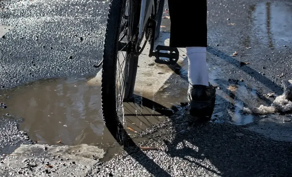 pothole in the road with water accumulated in it and a bicycle riding over it