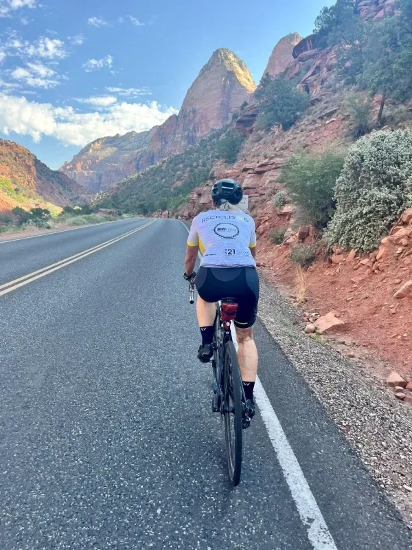 Rural Utah road without bike lane, narrow shoulder only with female cyclist riding near the white shoulder line.