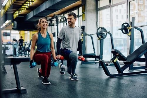 Strength Training happy couple at the gym doing lunges with dumb bells