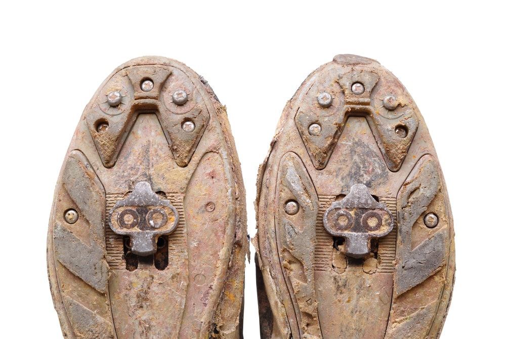 Two bolt mountain bike shoe cleat system shown on muddy cycling shoes