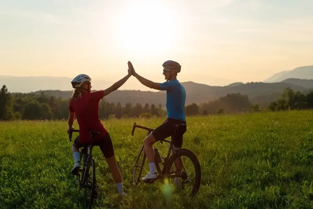 two road cyclists in a field grasping hands happily enjoying the outdoors together