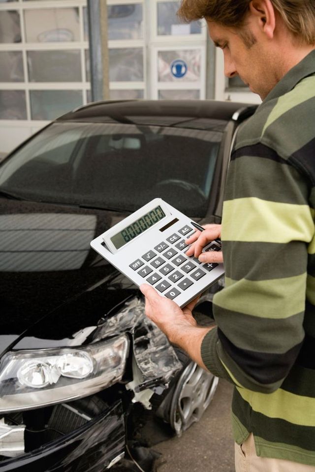 A man is holding a calculator in front of a damaged car.