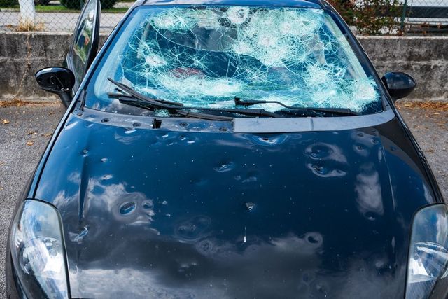 A black car with a broken windshield is parked in a parking lot.