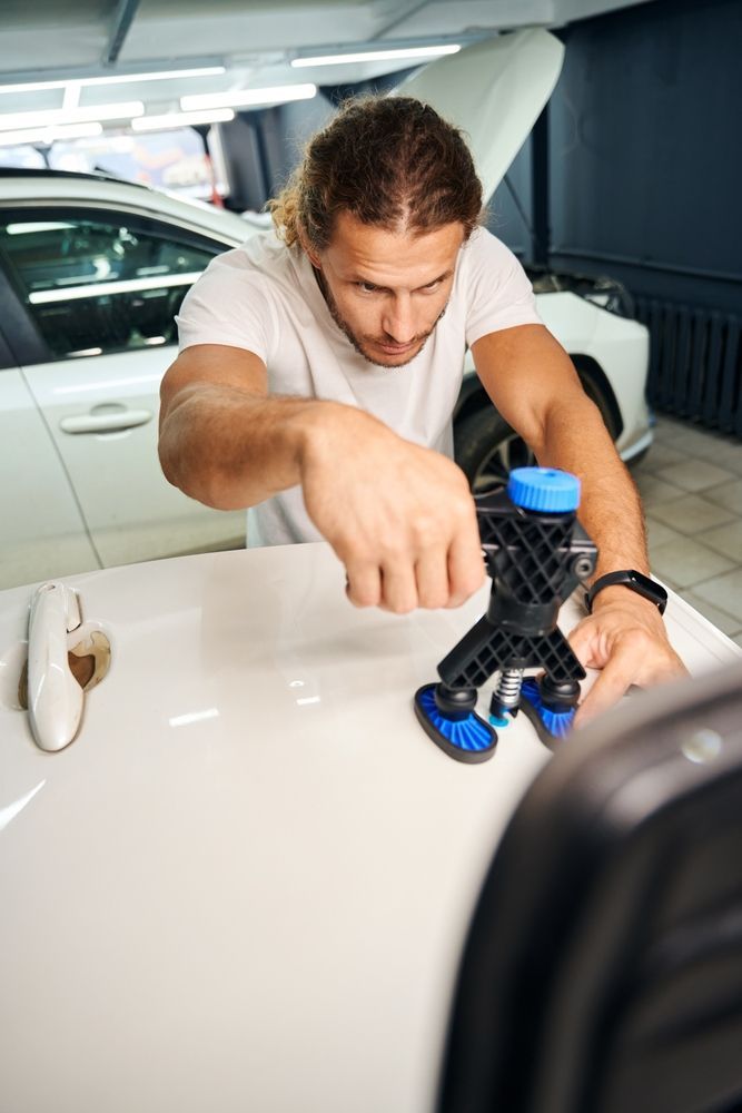 A man is using a tool to fix a dent on a car.