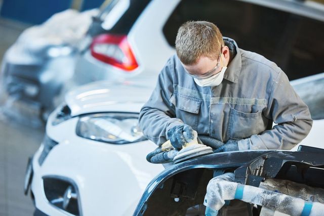 A man wearing a mask is sanding a car fender in a garage.