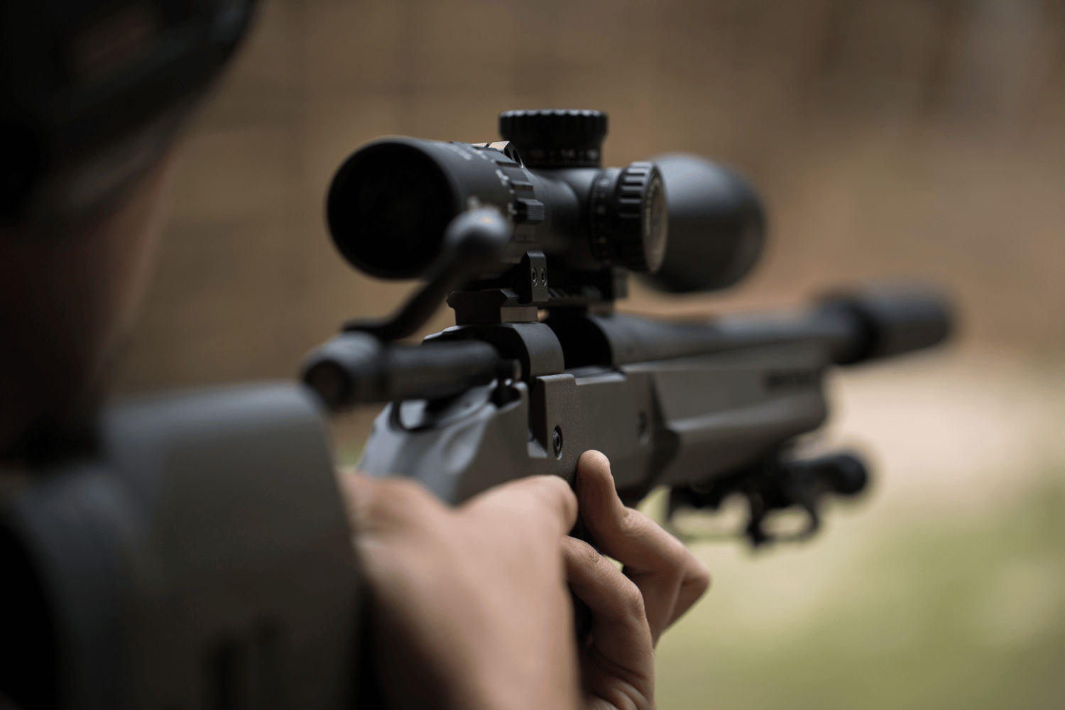 Person aiming a rifle with a scope in an outdoor setting