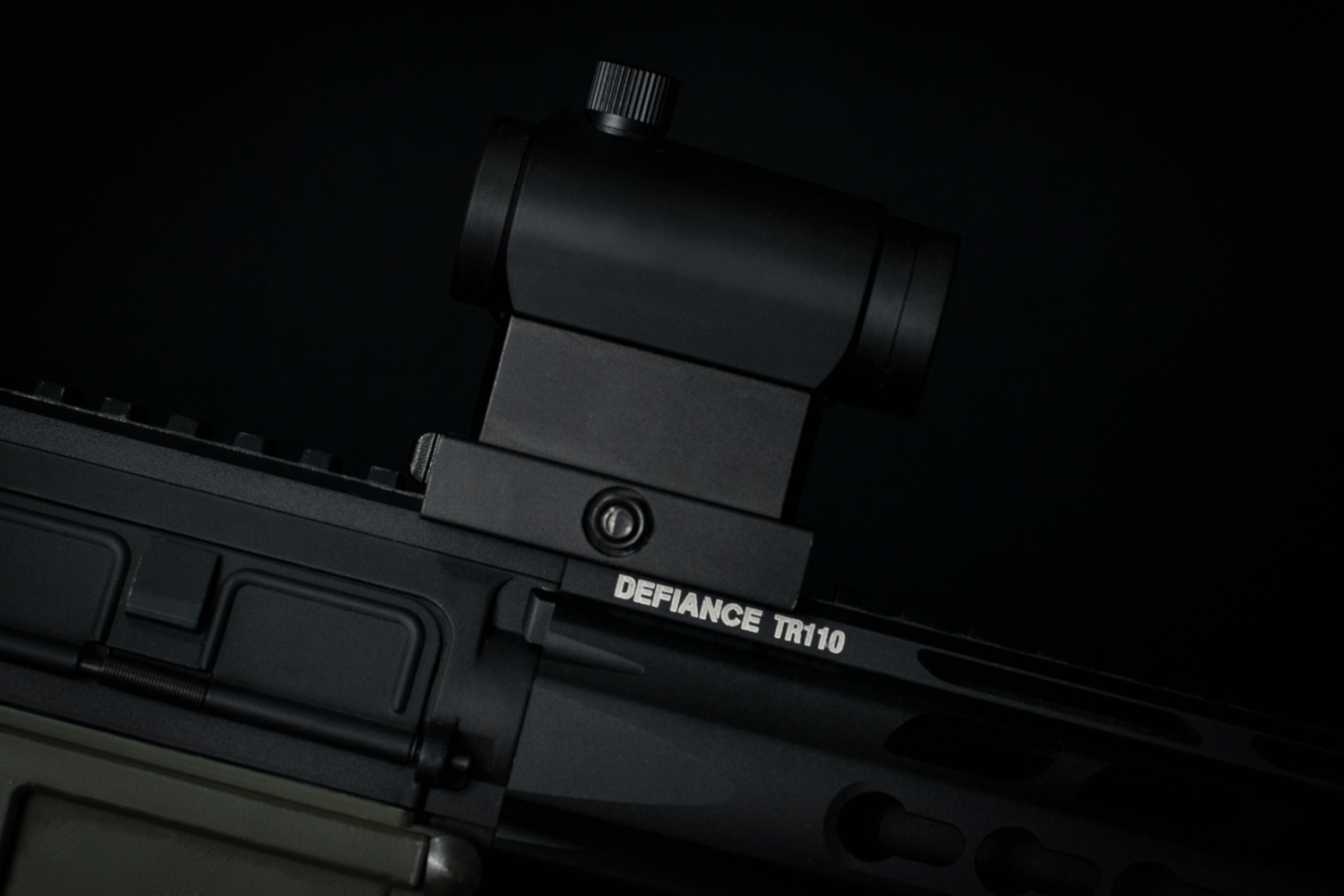 Black rifle with mounted red dot sight against a dark background
