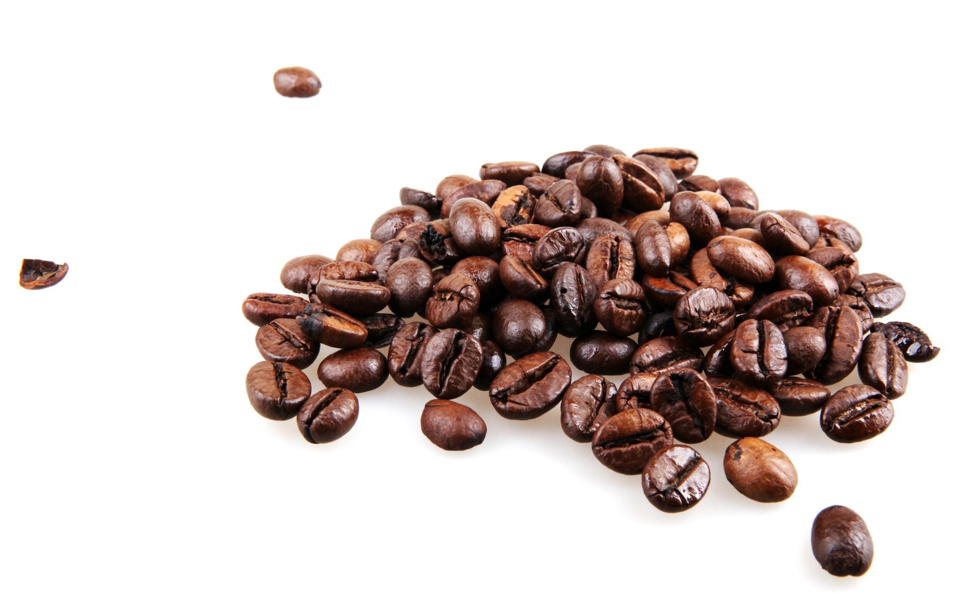 Chicchi di caffè tostati su una superficie bianca, alcuni sparsi.