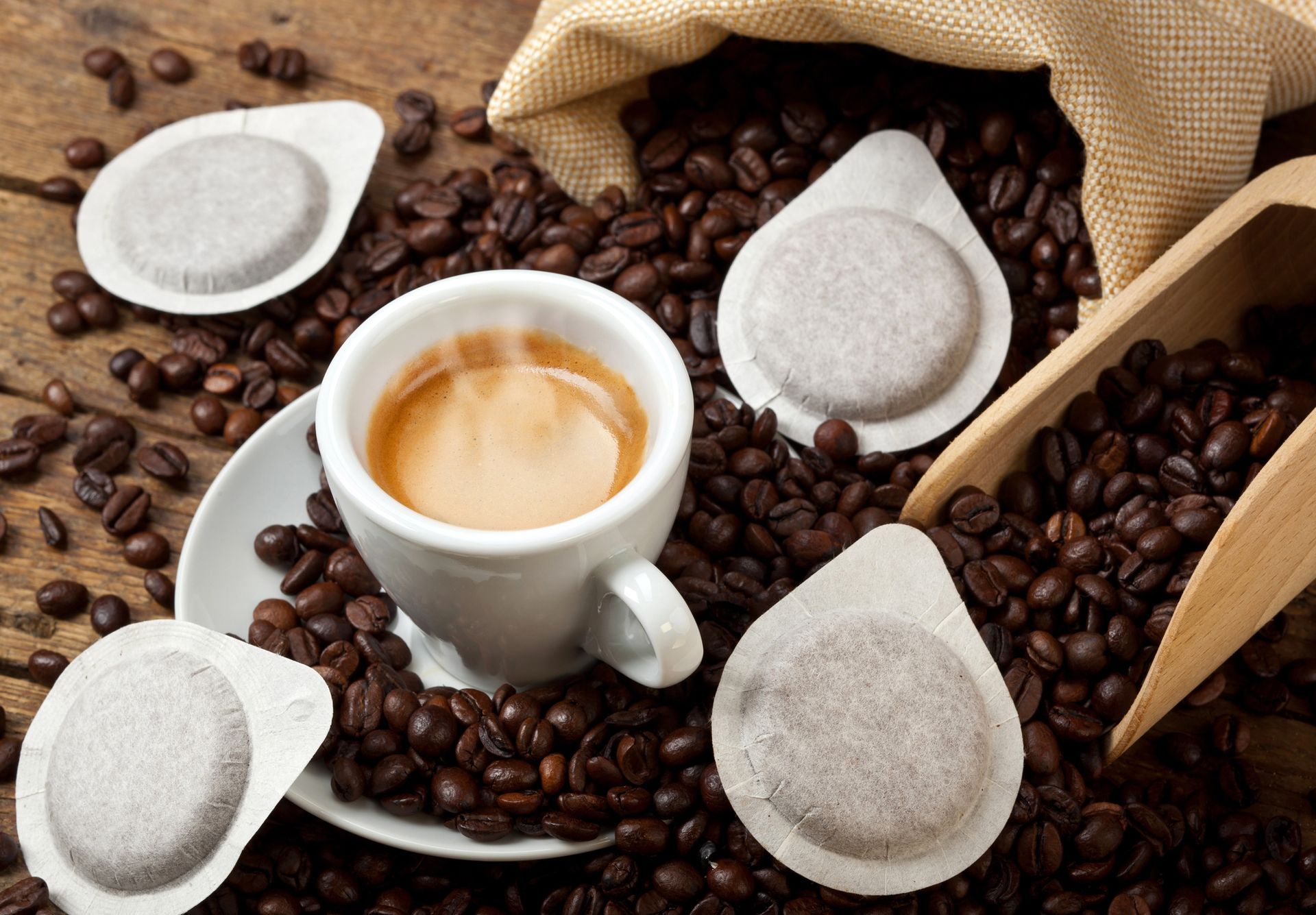 Tazza di caffè espresso con cialde e chicchi di caffè sparsi sul legno.